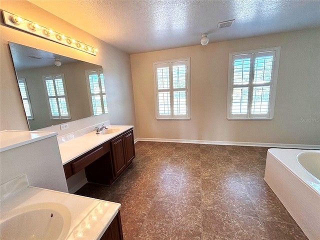 bathroom featuring vanity, a textured ceiling, a wealth of natural light, and a tub