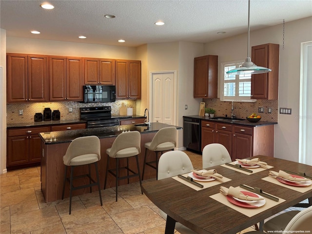 kitchen featuring hanging light fixtures, a kitchen island with sink, sink, and black appliances