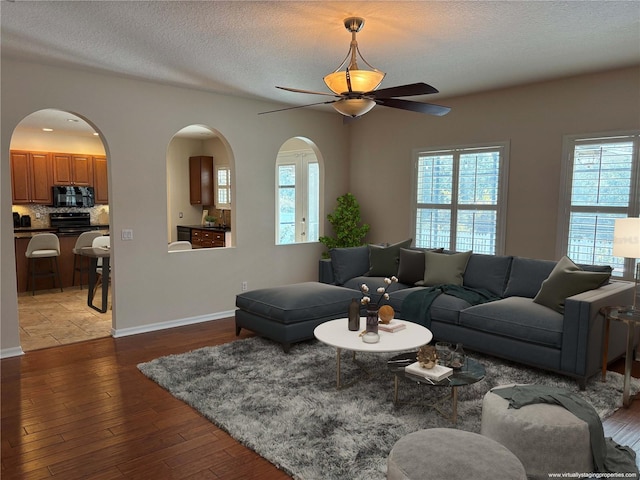 living room with a textured ceiling, ceiling fan, and dark hardwood / wood-style floors