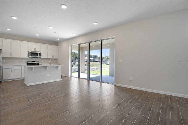 kitchen with dark hardwood / wood-style flooring, a center island with sink, white cabinets, and appliances with stainless steel finishes