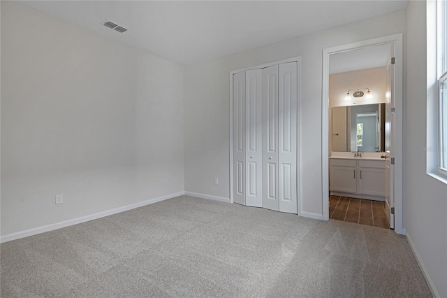 unfurnished bedroom with ensuite bath, a closet, sink, and dark colored carpet