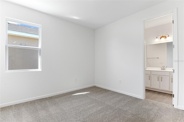 unfurnished bedroom with light colored carpet, sink, and ensuite bath