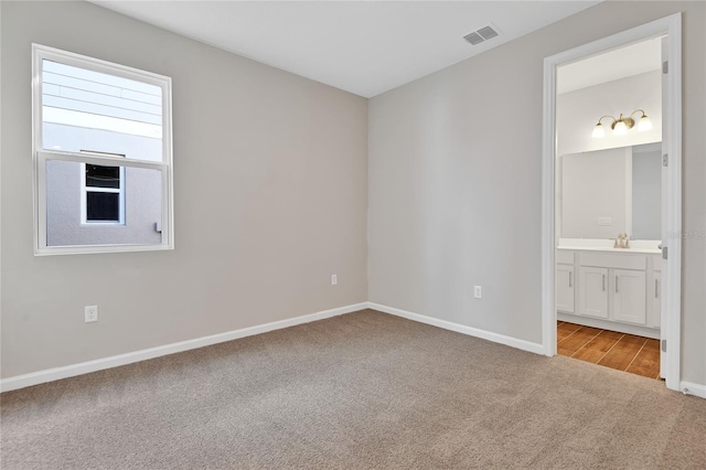 unfurnished bedroom featuring sink, light carpet, and connected bathroom