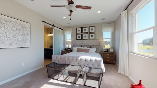 bedroom featuring ceiling fan, light colored carpet, a barn door, and ensuite bath