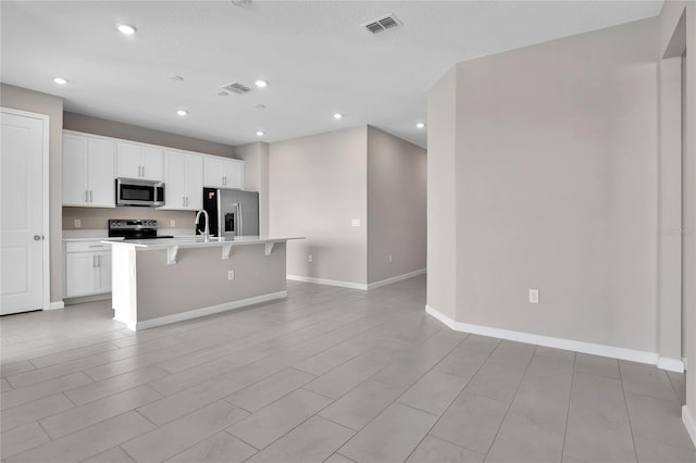 kitchen featuring a breakfast bar, sink, white cabinets, a kitchen island with sink, and stainless steel appliances