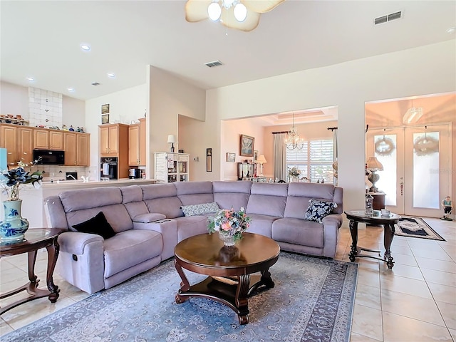 tiled living room featuring ceiling fan with notable chandelier and french doors