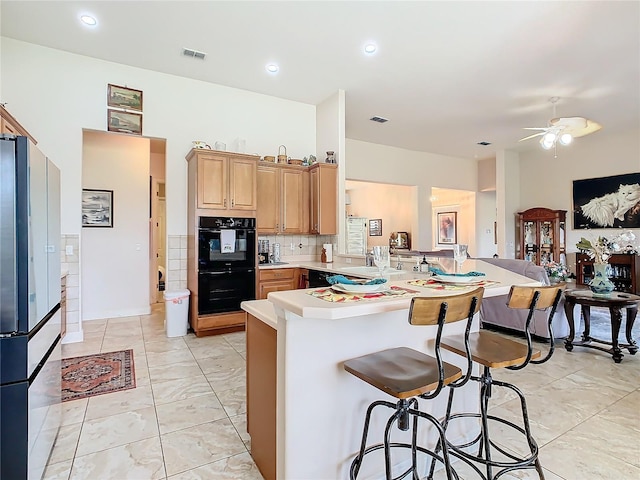 kitchen featuring ceiling fan, kitchen peninsula, double oven, backsplash, and a breakfast bar