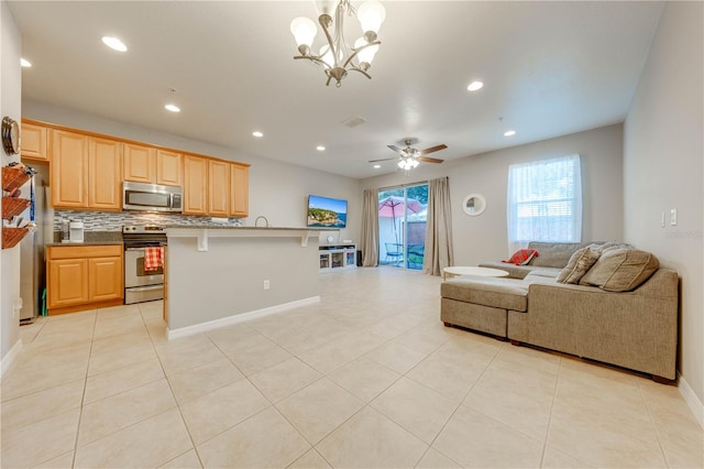 kitchen with a kitchen bar, tasteful backsplash, stainless steel appliances, ceiling fan with notable chandelier, and light tile patterned flooring