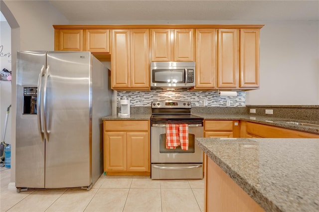 kitchen featuring tasteful backsplash, stainless steel appliances, sink, stone countertops, and light tile patterned floors