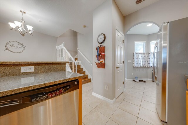 kitchen with appliances with stainless steel finishes, light stone counters, pendant lighting, light tile patterned floors, and a chandelier