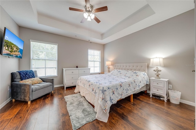 bedroom with ceiling fan, dark wood-type flooring, and a tray ceiling