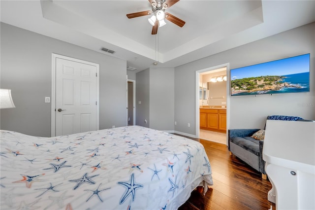 bedroom with connected bathroom, ceiling fan, hardwood / wood-style floors, and a tray ceiling