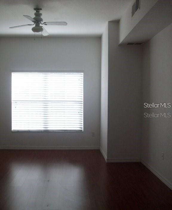 empty room with baseboards, dark wood finished floors, and a ceiling fan