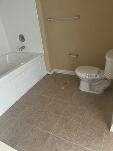 full bath featuring toilet, tile patterned flooring, baseboards, and a bath