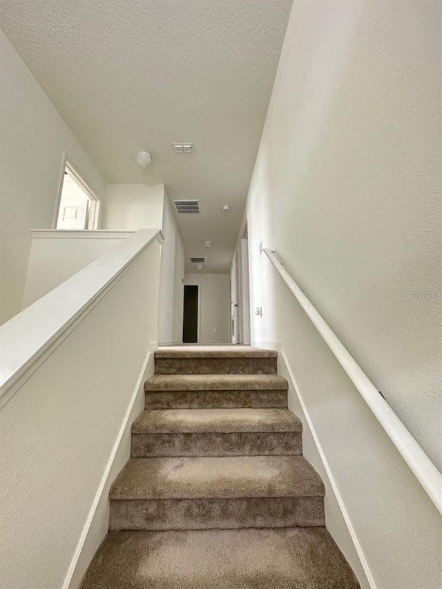 staircase featuring carpet and a textured ceiling