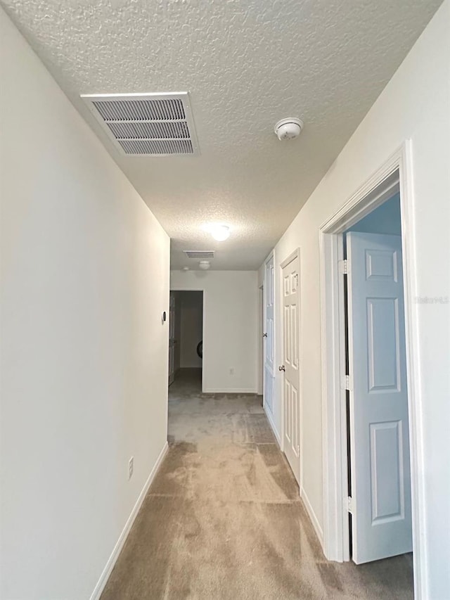 hall featuring light carpet and a textured ceiling