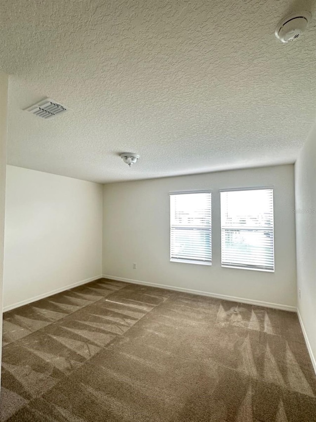 unfurnished room featuring dark colored carpet, a wealth of natural light, and a textured ceiling