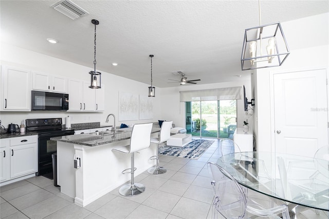 kitchen with light tile patterned floors, black appliances, ceiling fan, and a kitchen breakfast bar