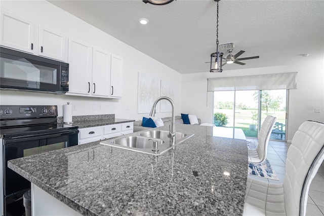 kitchen with black appliances, ceiling fan, sink, dark stone countertops, and a kitchen island with sink