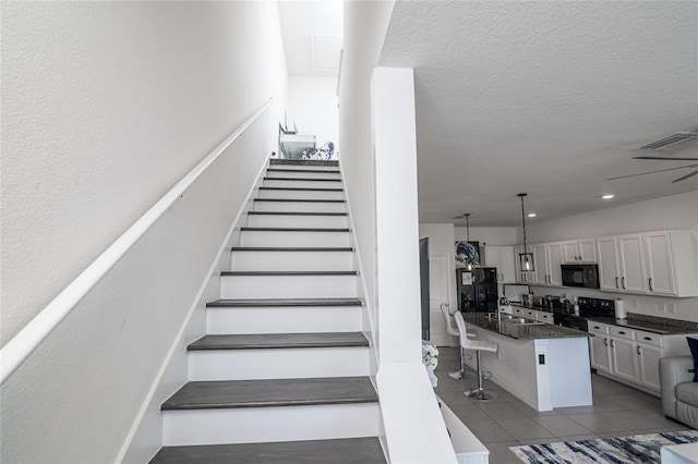 stairs featuring sink, light tile patterned floors, and a textured ceiling