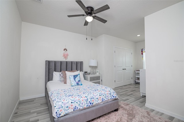 bedroom featuring a textured ceiling, a closet, light wood-type flooring, and ceiling fan