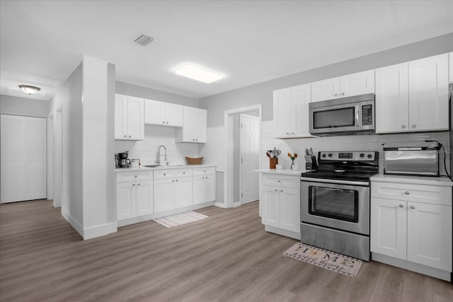 kitchen with white cabinetry, stainless steel appliances, light hardwood / wood-style flooring, and tasteful backsplash