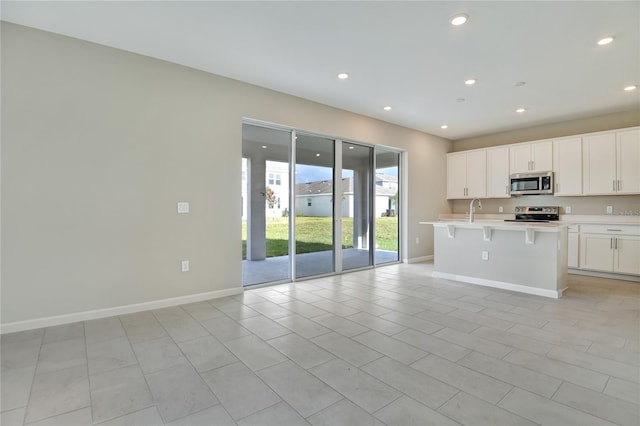 kitchen with a kitchen bar, sink, appliances with stainless steel finishes, a kitchen island with sink, and white cabinets