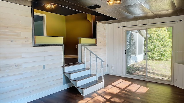 stairway with wood walls, hardwood / wood-style floors, and a drop ceiling