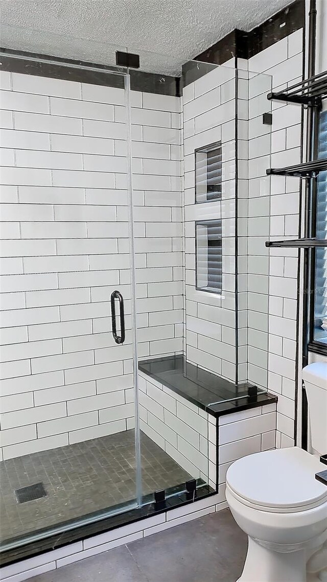 bathroom featuring toilet, a textured ceiling, and a shower with shower door