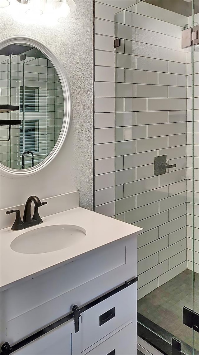 full bath with a textured wall, vanity, and a shower stall