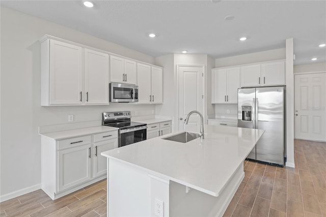 kitchen featuring sink, a breakfast bar area, stainless steel appliances, an island with sink, and white cabinets