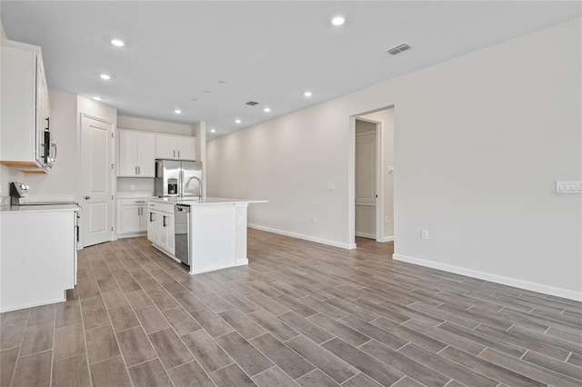 kitchen with sink, appliances with stainless steel finishes, white cabinets, and a center island with sink