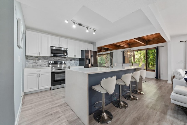 kitchen with decorative backsplash, appliances with stainless steel finishes, beam ceiling, light hardwood / wood-style floors, and track lighting