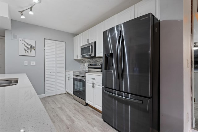 kitchen with stainless steel appliances, decorative backsplash, white cabinets, rail lighting, and light hardwood / wood-style flooring