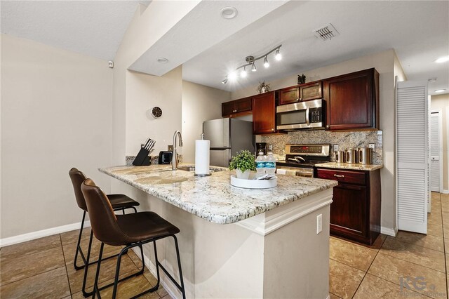 kitchen with kitchen peninsula, light stone countertops, tasteful backsplash, appliances with stainless steel finishes, and a kitchen breakfast bar