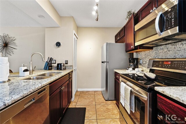 kitchen with appliances with stainless steel finishes, light stone countertops, light tile patterned floors, sink, and tasteful backsplash