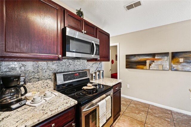 kitchen with backsplash, light tile patterned floors, light stone counters, and appliances with stainless steel finishes