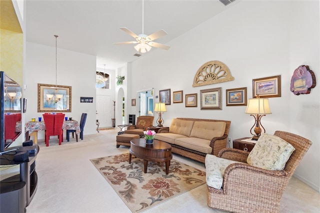 living room with a towering ceiling, light colored carpet, and ceiling fan with notable chandelier