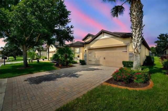 view of front of house with decorative driveway, stucco siding, an attached garage, stone siding, and a front lawn