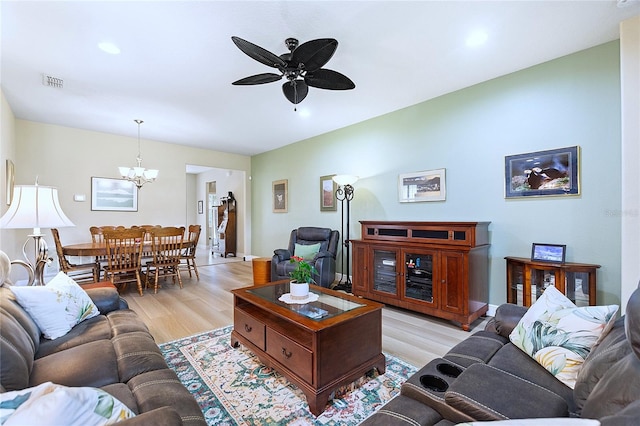 living area featuring baseboards, visible vents, light wood finished floors, and ceiling fan with notable chandelier