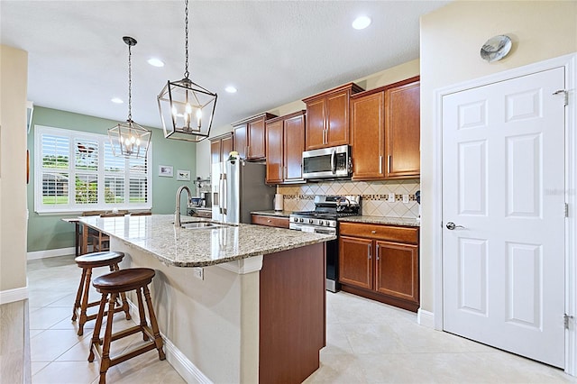 kitchen featuring a center island with sink, appliances with stainless steel finishes, a breakfast bar, hanging light fixtures, and a sink