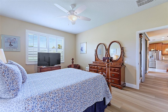 bedroom with stainless steel fridge, visible vents, baseboards, light wood-style flooring, and a textured ceiling