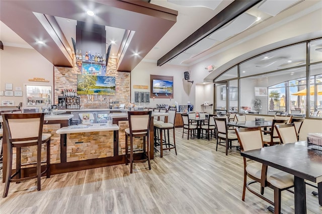 bar featuring light wood finished floors, indoor wet bar, beam ceiling, and crown molding