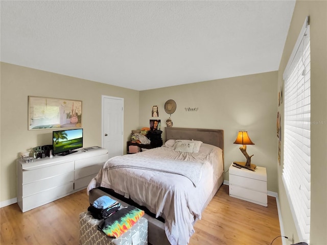 bedroom with a textured ceiling, baseboards, and wood finished floors