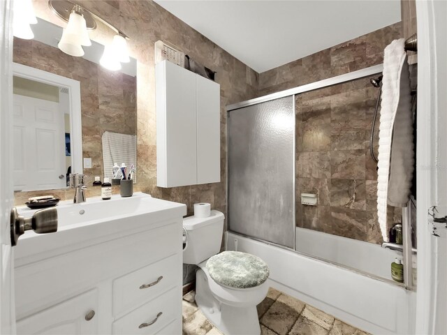 full bathroom featuring toilet, tile patterned flooring, enclosed tub / shower combo, tile walls, and vanity