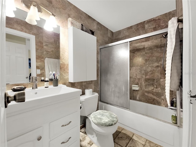 full bath featuring toilet, combined bath / shower with glass door, vanity, and tile walls