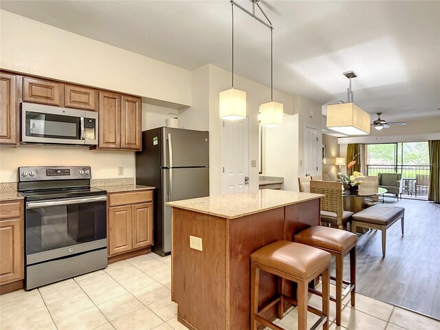 kitchen featuring a breakfast bar, light tile patterned floors, stainless steel appliances, light stone counters, and ceiling fan