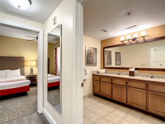 bathroom with ceiling fan with notable chandelier, a textured ceiling, tile patterned floors, and dual bowl vanity