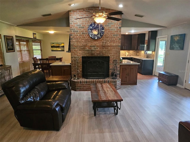 living room with light wood-type flooring, a brick fireplace, lofted ceiling, and sink