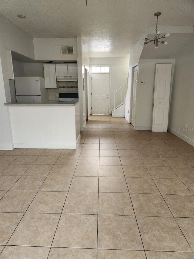 kitchen featuring tasteful backsplash, white fridge, white cabinetry, a textured ceiling, and light tile patterned floors